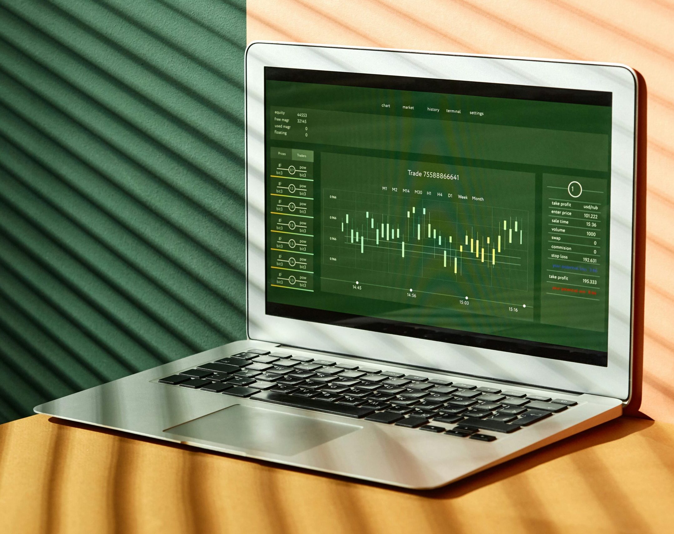 A laptop displaying stock market data with shadows from window blinds casting dramatic patterns.